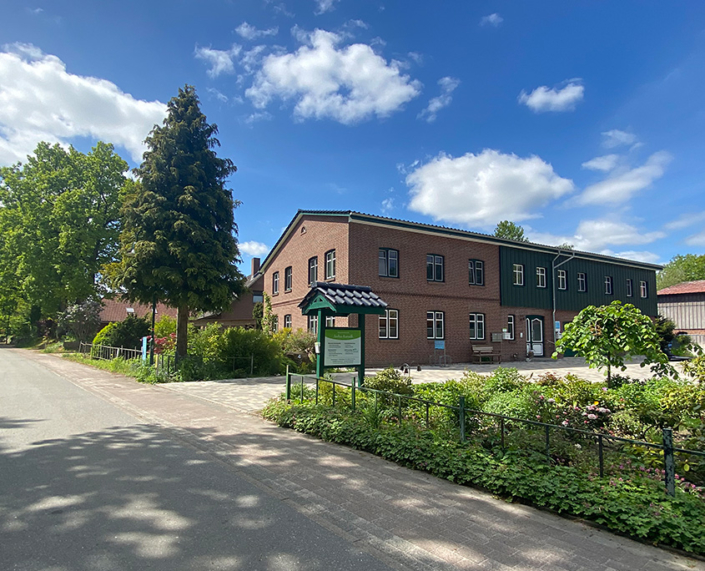 Die Praxis von Andrea Kunrath von aussen mit Praxisschild, großem Hof und viel Grün